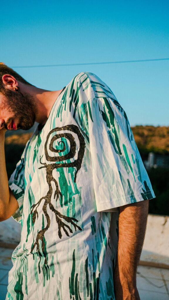 Young man with beard posing outdoors in a white Customised Printed T-Shirt under a clear blue sky, highlighting unique personal style and creativity.